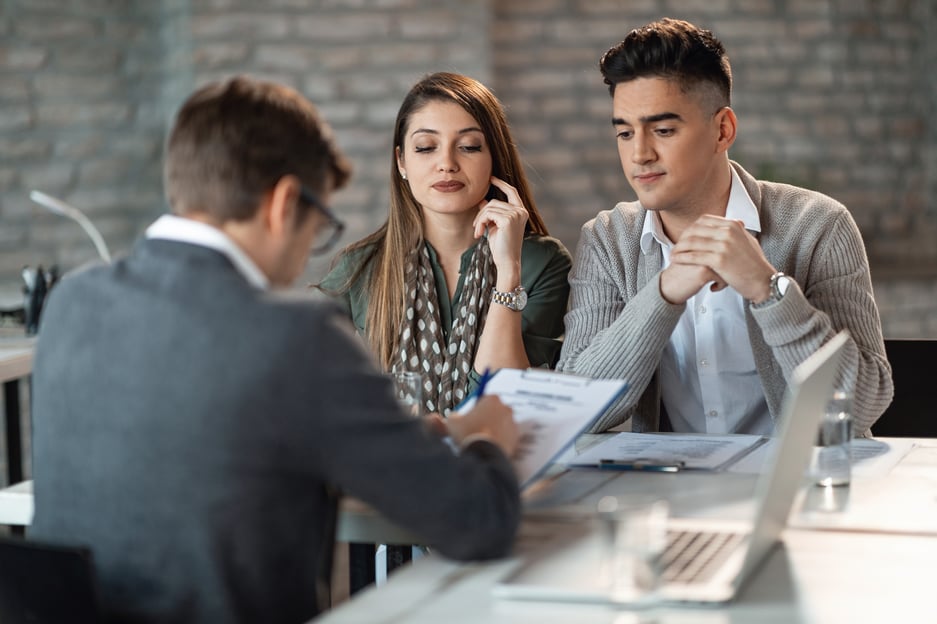 Imagen de una pareja joven y el gerente del banco en una reunión, discutiendo y creando un plan de pago para un préstamo. La imagen representa un compromiso financiero y la importancia de establecer acuerdos claros y realistas para el reembolso del préstamo.