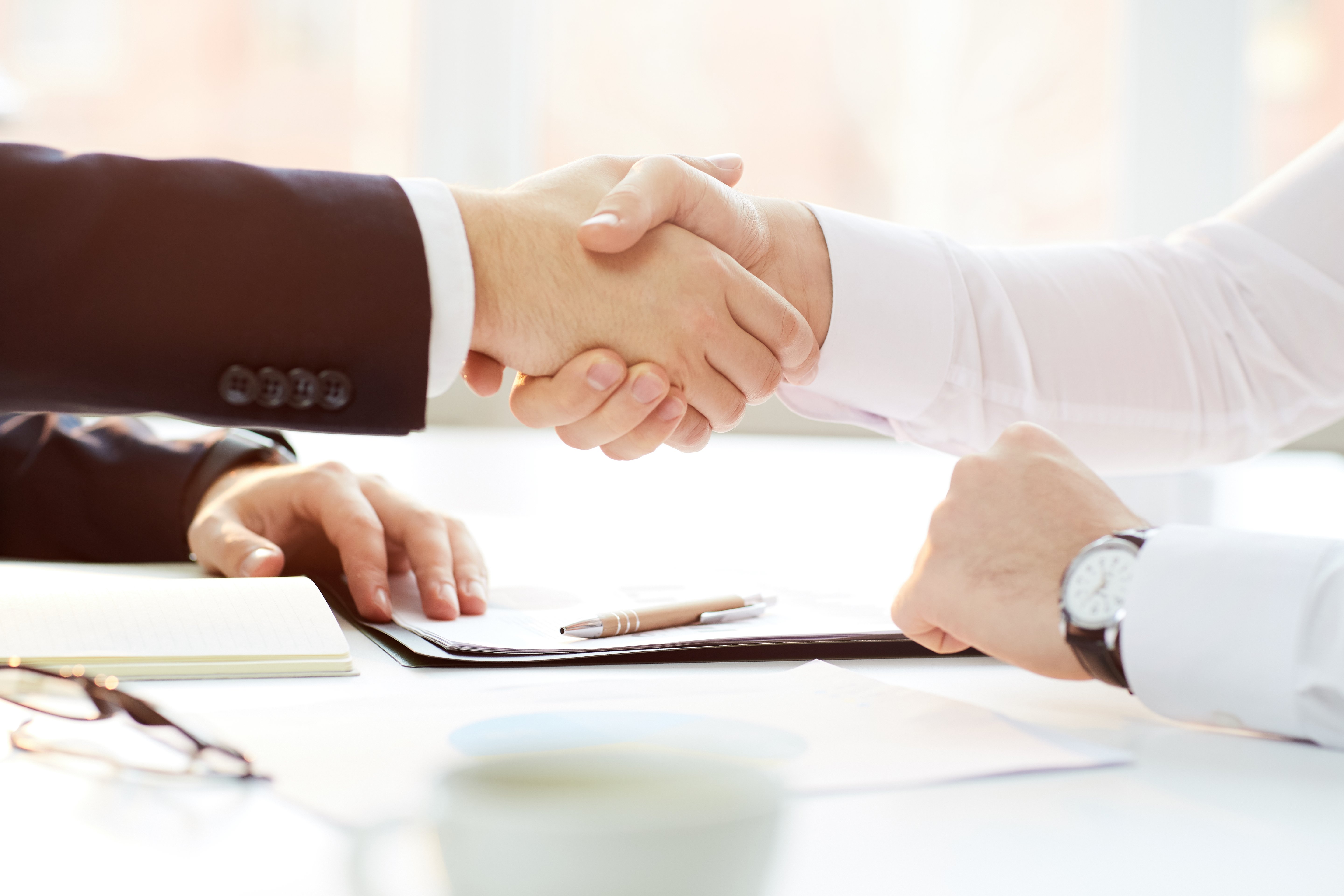 Primer plano de un hombre de negocios sentado a la mesa y estrechando la mano de un nuevo Angel Inversor tras la firma del contrato